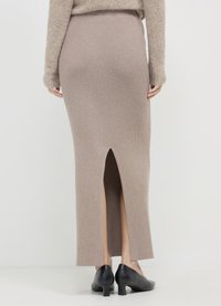 Jupe maxi en maille beige avec une fente à l'arrière, associée à des chaussures noires à petit talon. Caractérisée par une texture côtelée et une silhouette ajustée.
