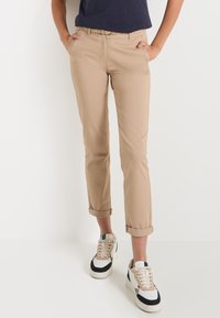 Pantalons beiges fuselés avec ourlets retroussés, en mélange de coton. Dotés de poches avant et associés à des baskets blanches et noires.