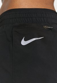 Pantalones cortos deportivos negros con una cinturilla elástica, que cuentan con un bolsillo con cremallera y un logo de Nike blanco reflectante en el lateral.