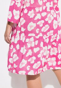 Rosa Kleid mit einem gestuften Design, das ein kräftiges weißes und hellrosa Leopardenmuster aufweist. Kurze Ärmel und leichtes Material mit einer leicht strukturierten Oberfläche.