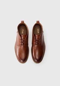 Chaussures en cuir marron avec une texture lisse, un design à lacets et des accents cousus sur les côtés. Dotées d'un bout rond et d'une petite boucle au talon.