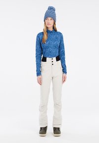 Modrá vzorovaná blúzka s dlhým rukávom, off-white nohavice s čiernym pásom a gombíkmi. Model má na sebe pletenú modrú čiapku a zelené topánky.