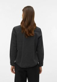 Czarna koszula z długim rękawem wykonana z denimu, z zaokrąglonym dołem, subtelnym przeszyciem i mankietami na guziki. Brak widocznych wzorów czy detali metalowych.