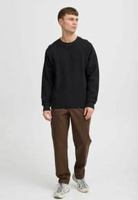 Pulover negru texturat cu guler rotund și mâneci lungi, asortat cu pantaloni lejeri maro și pantofi sport gri deschis.