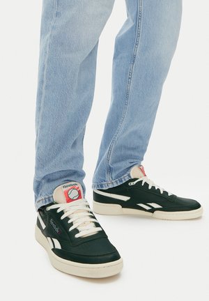 Čierne kožené tenisky s bielymi detailmi, krémovými podrážkami a logom Reebok. V kombinácii so svetlo modrými džínsy s uvoľneným strihom.