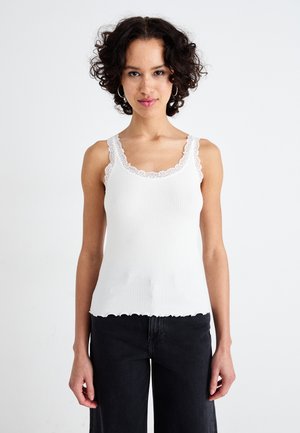 Witte geribbelde tanktop met geschulpte zoom en kantafwerking langs de halslijn en bandjes. Het materiaal lijkt zacht en aansluitend.