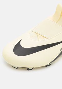 Scarpette da calcio giallo chiaro con superficie testurizzata, caratterizzate da un logo Nike nero e una fascia elastica. Progettate per le prestazioni con tacchetti moldati.