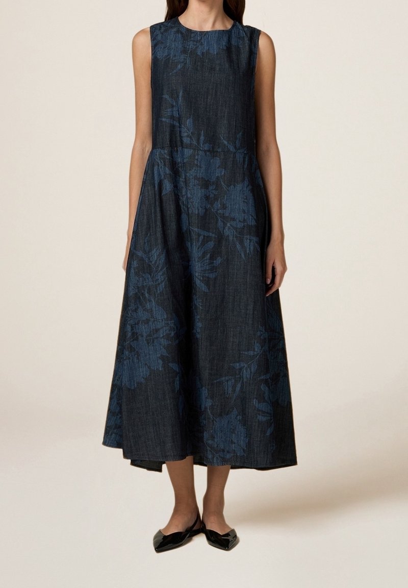 Robe midi sans manches bleu foncé à motif floral, ajustée à la taille, portée avec des ballerines slingback noires à bout pointu sur fond clair.