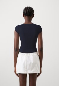 Mörkblå ribbad kortärmad topp med en figurnära passform, kombinerad med en vit denim-minikjol. Mjuk textur och minimalistiska designdetaljer.