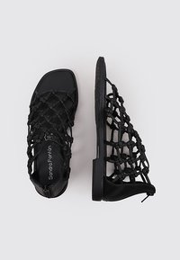 Sandalias negras con un diseño de tiras trenzadas, suela plana y cremallera lateral. Cuentan con una plantilla texturizada para mayor agarre y comodidad.