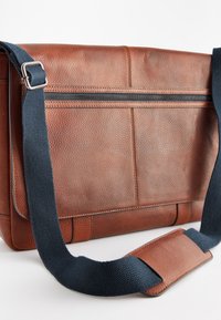 Geantă de mesagerie din piele maro cu o suprafață texturată, prevăzută cu o curea reglabilă de culoare albastru închis și un buzunar cu fermoar în față.