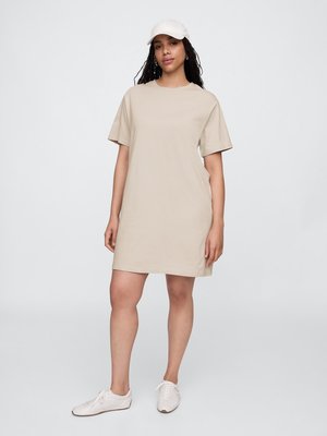 Robe en coton beige à manches courtes avec une coupe décontractée, un col rond et une texture lisse. Assortie à une casquette blanche et des baskets.