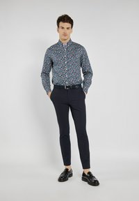 Koszula w kwiatowy wzór o granatowym tle, z długimi rękawami i kołnierzykiem zapinanym na guziki; zestawiona z granatowymi spodniami w slim fit i czarnymi mokasynami.