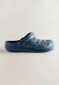 Blå plastklack med ventilationshål, upphöjda kanter och ett band. Texturerad yta och rund tådesign. Gummisula för grepp.