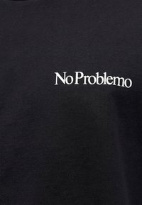 Μαύρο ύφασμα με λευκό κείμενο "No Problemo" τυπωμένο ελαφρώς γωνιακά με απλό serif γραμματοσειρά.