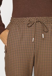 Pantalon à carreaux marron avec une taille élastique munie d'un cordon de serrage, des poches latérales et un tissu doux et texturé.