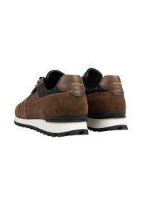 Brown suede and leather sneakers with black accents. Features a white sole and yellow back detail. Textured upper with lace-up design.