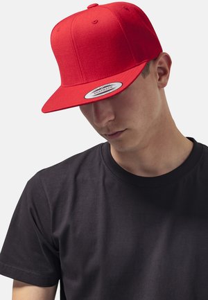 Cappellino snapback rosso con visiera piatta e design a sei pannelli, realizzato in tessuto, con etichetta sul davanti. Indossato con una maglietta nera.