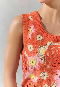 Virkattu toppi, jossa on kukkakuosi oranssina, vaaleanpunaisena, kermanvärisenä ja keltaisena. Pääntie on ribbireunainen ja siinä on avonainen neulekuvio.