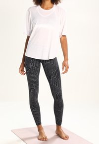 Top blanco de manga corta con diseño texturizado, combinado con leggings negros que presentan líneas y patrones geométricos blancos.