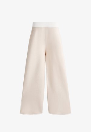 Pantalons à jambes larges en tissu beige clair et doux, avec une taille blanche côtelée et des lignes épurées, sans fermetures ni poches visibles.