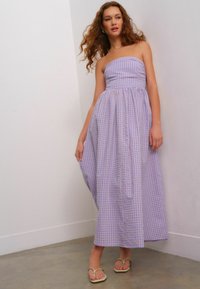 Abito maxi senza spalline in un leggero motivo a quadri viola e bianco, con un corpetto aderente e una gonna fluente. Indossato con infradito color cammello.