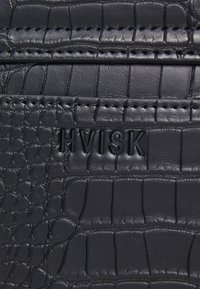 Svart texturerad läderhandväska med krokodilsmönster, med präglad varumärkeslogotyp "HVISK" och kontrasterande sömmar.