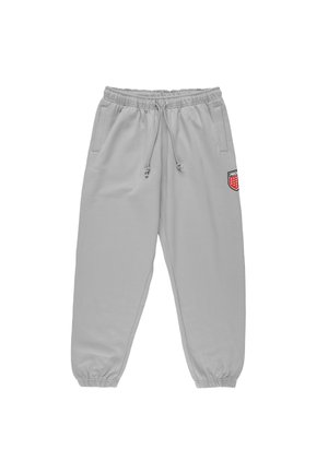 Jasnoszare spodnie dresowe z elastycznym pasem i mankietami, ściągaczem, bocznymi kieszeniami oraz małą czerwoną naszywką w kształcie tarczy na prawej udzie.