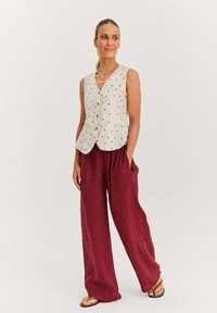 Biały leniasty kamizelka w czerwone kropki, z dekoltem w serek i kieszeniami, w zestawieniu z luźnymi burgundowymi spodniami o szerokich nogawkach.