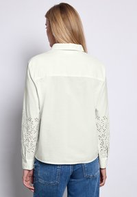 Camisa blanca de botones con detalles de ojal en las mangas y el cuello, de corte recto, combinada con vaqueros de mezclilla azul.