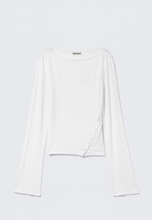 White long-sleeve top made of soft fabric. Features rounded neckline, side button detail, and a cropped silhouette. Smooth texture, casual design.