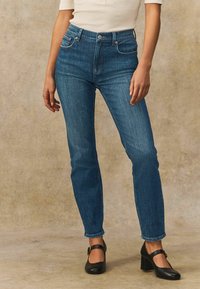 Hög midja blå denim jeans med smal passform, med framfickor och knappstängning, i kombination med svarta Mary Jane-klackar.