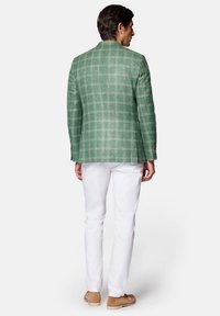 Zielona marynarka w kratę z teksturowanej tkaniny, zaprezentowana od tyłu. W połączeniu z białymi spodniami i jasnobrązowymi butami.