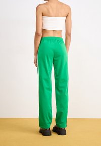 Pantalones deportivos verdes hechos de tela suave, con un ajuste relajado, cinturilla elástica y franjas blancas a los lados. Estilizados con zapatos negros gruesos.