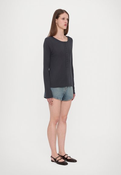 Langärmliges dunkelgraues Hemd mit Knopfleiste, kombiniert mit hellen Jeansshorts und braunen flachen Schuhen. Glattes Material, lockere Passform.