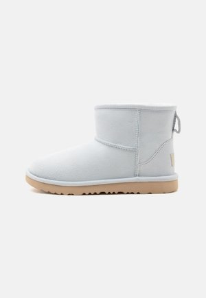 Bottine en daim gris clair avec semelle en caoutchouc beige et languette à l'arrière, montrée de profil sur un fond neutre.