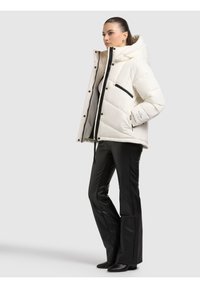 Biała puchowa kurtka z pikowanym wzorem, czarnymi akcentami i kapturem, zestawiona z dopasowanymi czarnymi skórzanymi spodniami i botkami za kostkę.