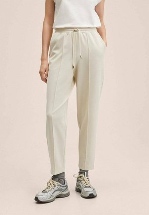 Lichtbeige joggers met elastische taille en trekkoord, voorzien van zijnaden en een taps toelopende pijp, gecombineerd met grijze sportschoenen.