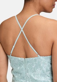 Robe brodée bleu clair avec des fines bretelles croisées et un corsage texturé. Présente des motifs floraux et une fermeture éclair au dos.