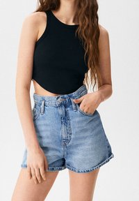 Černý žebrovaný crop top s kulatým výstřihem, spárovaný s svetle modrými džíny s vysokým pasem, které mají ohrnuté lemování a přední kapsy.