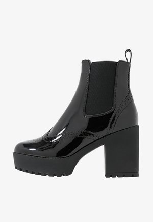 Bottes de cheville en cuir verni noir avec une semelle épaisse et un talon haut, dotées de panneaux latéraux en élastique et de détails de couture décoratifs.