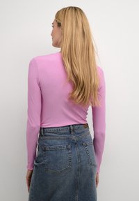 Haut ajusté à manches longues en tissu côtelé rose clair, associé à une jupe en denim foncé taille haute avec poches et détails de couture.