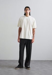 Világos bézs, túlságosan nagy póló, raglán ujjal, fekete, bő szárú nadrággal párosítva. Karcsú fekete sportcipők egészítik ki a megjelenést.