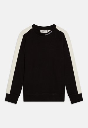 Svart hettegenser med lange ermer, kremfarget sidestrek, rund hals, og Calvin Klein-merke ved halsen, laget av mykt materiale.