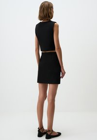 Top corto nero con design senza maniche abbinato a una mini gonna nera. Tessuto morbido, linee semplici e estetica minimalista.