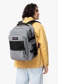 Mochila Eastpak gris con múltiples compartimentos con cremallera, bolsillo frontal de malla, correas ajustables y un exterior de tela duradera.