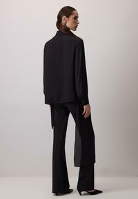 Czarna, d�ługorękawowa koszula z kołnierzykiem o luźnym kroju, w zestawie z pasującymi spodniami. Gładki materiał z lekkim połyskiem, zwężający się krój nogawek.