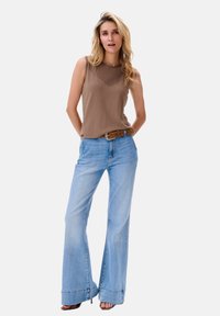 Bruine mouwloze top met een gestructureerd patroon en lichtblauwe hoge taille flared jeans, met een riem en hakken.