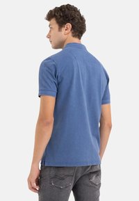 Camisa polo azul para hombre hecha de algodón, con mangas cortas, un cuello y una textura suave. La vista trasera muestra una costura trasera discreta.