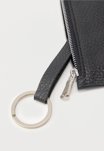 Κοντινό πλάνο μαύρου δερμάτινου πορτοφολιού με υφή, με ασημένιο φερμουάρ και προσαρτημένο ασημένιο μπρελόκ σε μαύρο λουράκι.